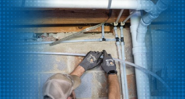 A plumber working on water line connections in a residential setting.