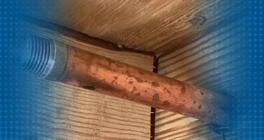 A plumber repairing a leaking pipe with water droplets visible.