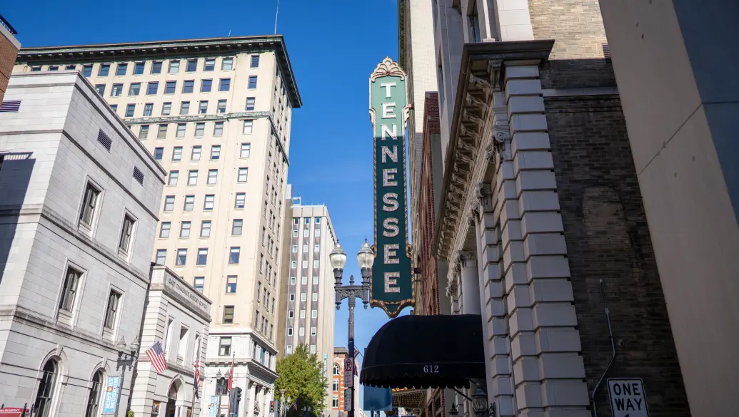 Green sign that says Tennessee with city buildings in background.