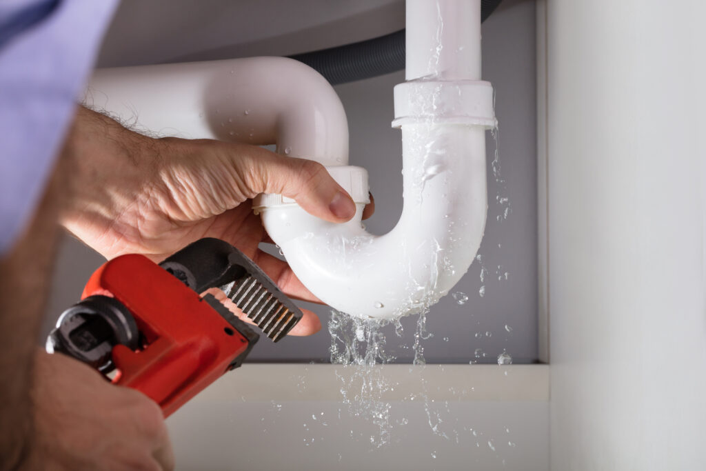 Close-up of plumber fixing white sink pipe with red adjustable wrench