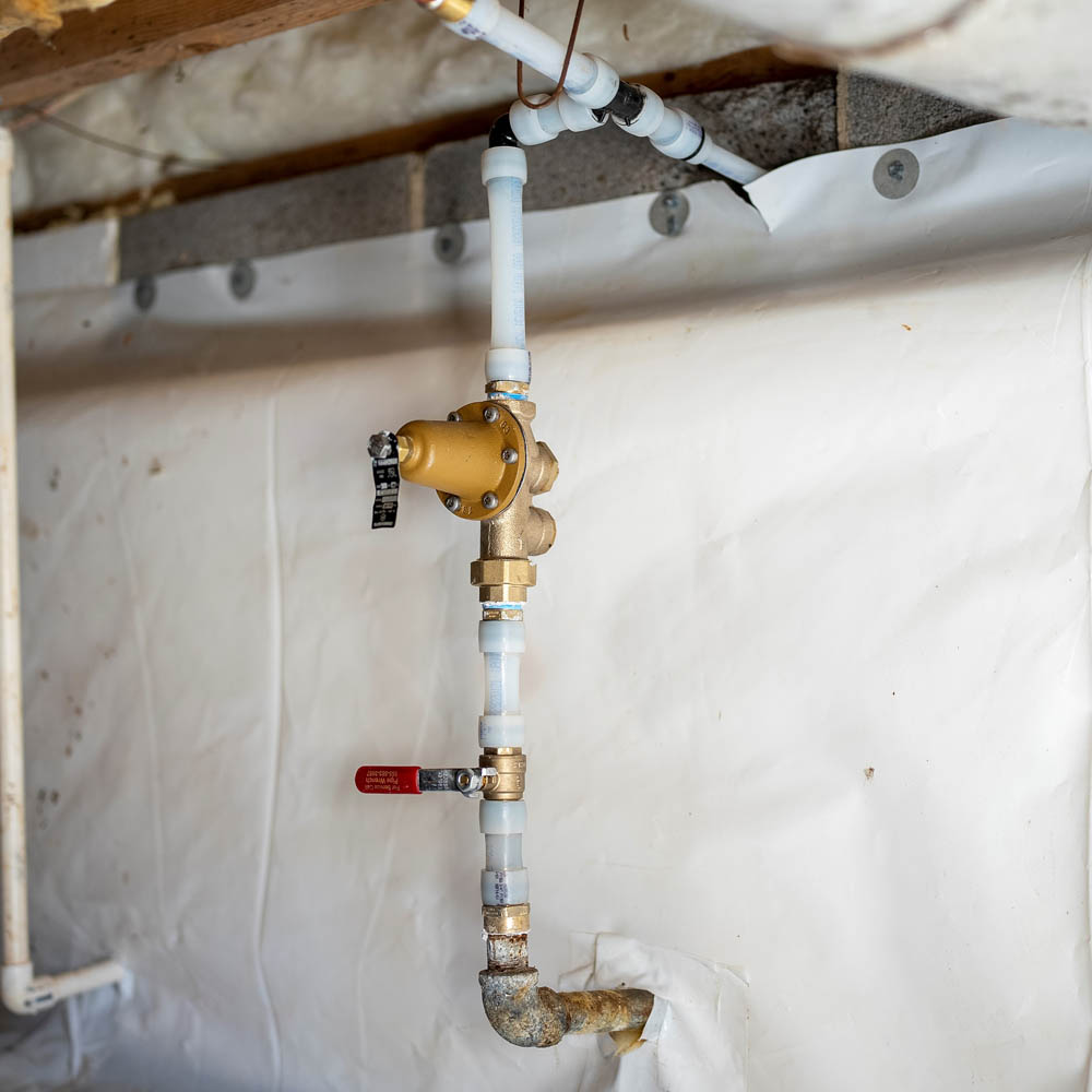 Plumbing pipes coming out of a basement wall.