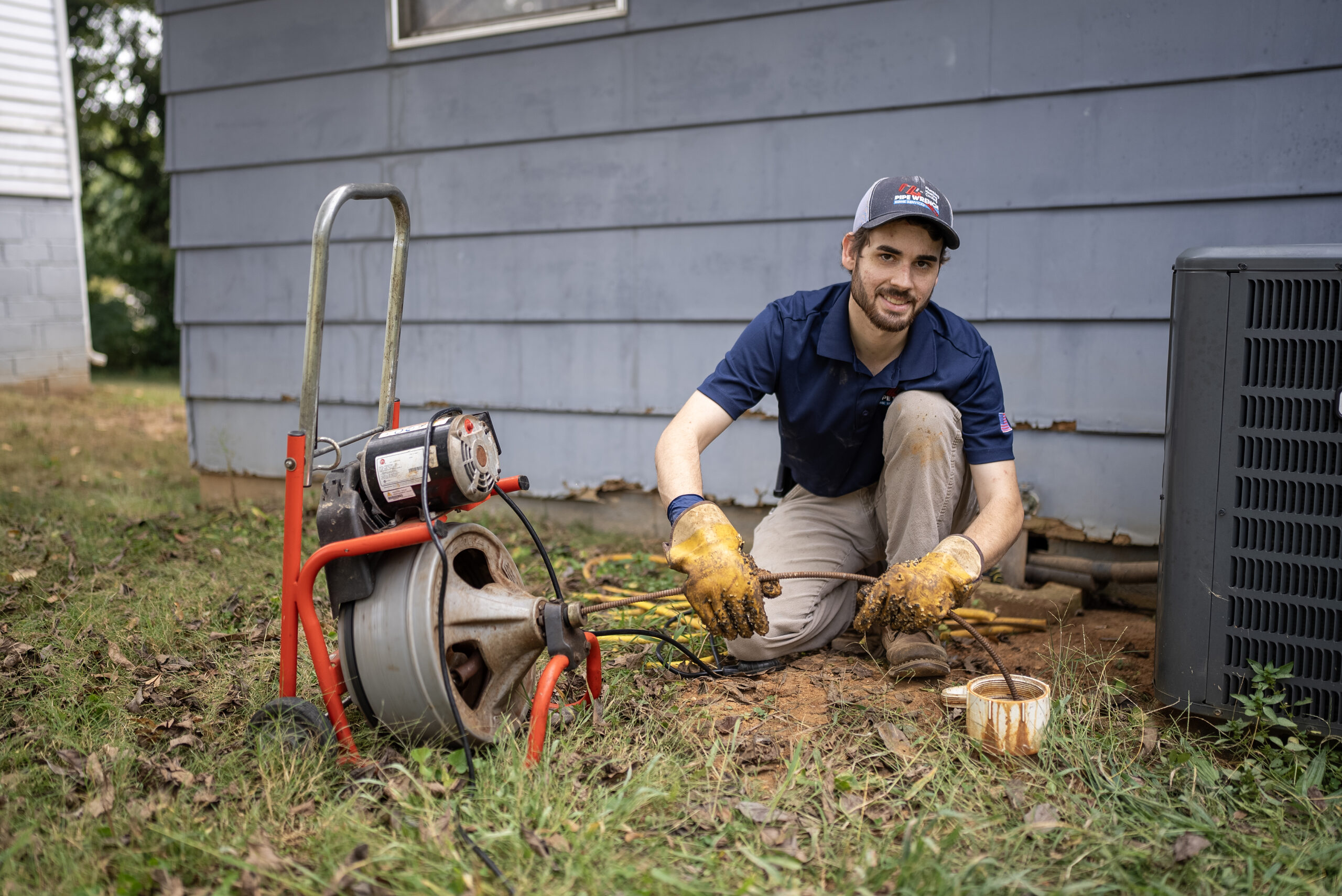 Technician kneeling in yard, performing a drain cleaning