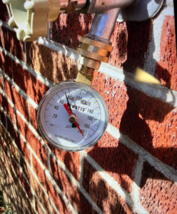 A water pressure gauge on the side of a brick house